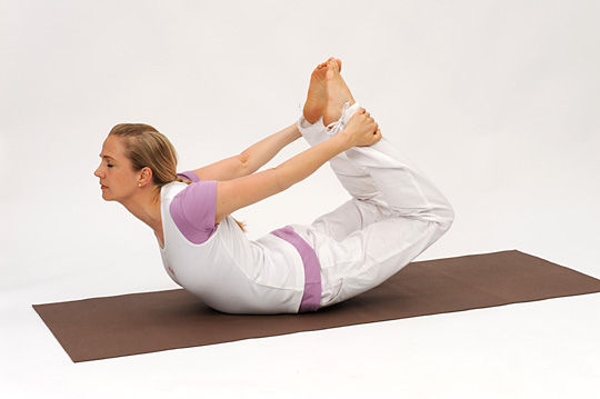 <b>BOW (DHANURASANA)</b> – This asana gives a full backward bend to the entire spine, producing great benefits from the cervical through thoracic, lumbar and sacral regions. It gives the combined effect of the Cobra and locust. The digestive organs are massaged and invigorated, it helps to remove constibation and gastro-intestinal disorders. The Bow helps to reduce fat and relieve congestion of the blood in the abdominal viscera.